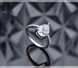Macro detail of pear-cut diamond ring in silver featuring micro-pave flower accents