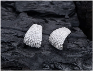 Detail of pavé-set crystals on curved silver stud earrings over charcoal background