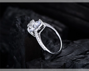 Close-up of elegant silver ring with large round solitaire and pave diamonds on black stone