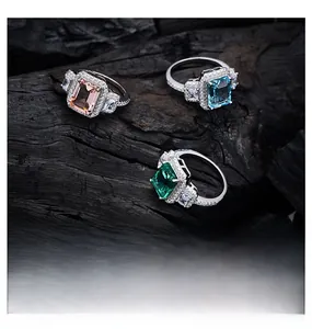Close-up of rectangular emerald cut rings with halo pavé diamonds on dark charcoal wood