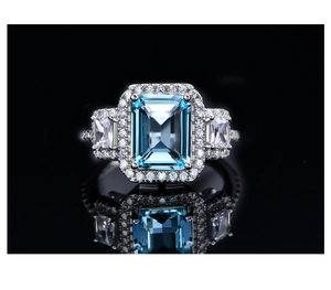 Macro shot of emerald-cut blue gemstone ring with surrounding diamonds on black surface