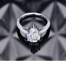 Macro detail of pear-cut zircon silver ring with floral accents on reflective glass