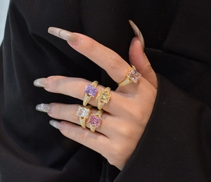 Close-up of five colorful princess cut diamond rings worn on a hand against black background