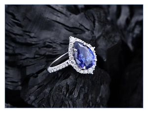 Macro shot of pear-shaped blue sapphire ring with cluster diamonds on black charcoal