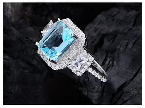 Macro detail of emerald-cut blue gemstone ring with sparkling diamond halo setting