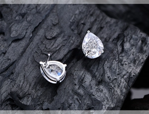 Detailed view of pear-cut crystal stud earrings with flower motif on black wood background
