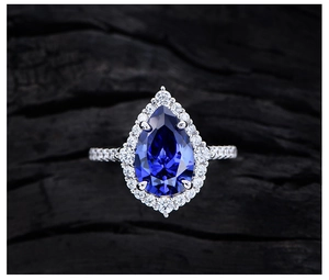 Macro shot of pear-cut blue tanzanite ring with halo diamonds on black wood