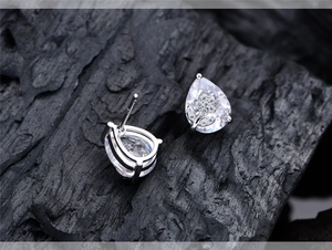 Close-up of pear-cut sterling silver floral studs with diamonds on dark wood background