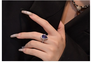 Detail of pear-cut blue sapphire silver ring worn on model with elegant halo setting