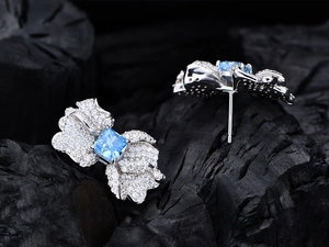 Vista macro di orecchini a farfalla in argento con gemma blu su legno scuro