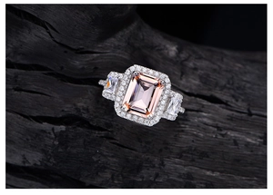 Macro shot of emerald cut pink gemstone ring with white side stones on dark wood