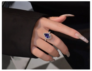 Macro detail of pear-shaped tanzanite blue ring with halo diamonds on model's hand