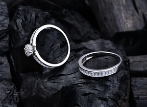 Close-up of two S925 silver rings with square zircon stones on charcoal wood background