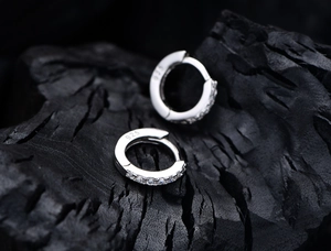 Macro shot of S925 sterling silver huggie earrings with inset cubic zirconia on black rock