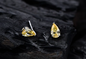 Macro shot of pear-cut yellow gemstone earrings with silver three-prong setting on charcoal