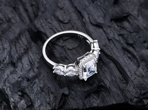 Detail of emerald cut gemstone ring with marquise accents on dark stone background