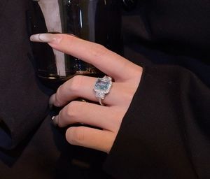 Close-up of emerald-cut light blue gemstone ring with cluster setting on model hand