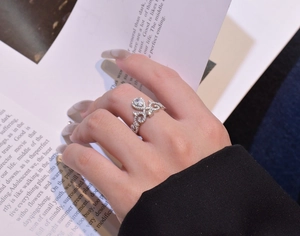 Detail of silver crown ring with pear-shaped cubic zirconia worn by model over book