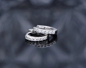 Detail of silver hoop earrings with white zircon stones on a dark reflective surface