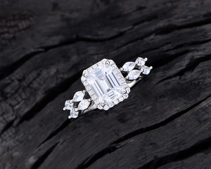 Macro view of emerald-cut white diamond ring with marquise side stones on charcoal wood