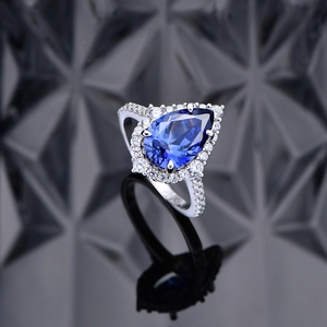 Elegant pear-cut blue sapphire silver ring with halo diamonds on dark background