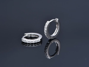 Macro shot of silver hoop earrings with clear cubic zirconia on a dark mirror base