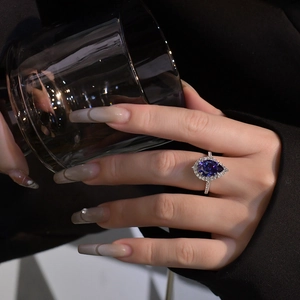 S925 silver pear cut tanzanite halo engagement ring shown held against a glass