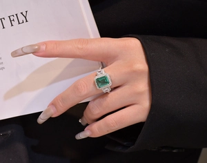 Close-up of an emerald-cut green stone ring with diamond halo on a model's hand