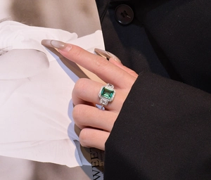 Fashionable emerald cut green gemstone ring with halo diamonds on a model hand