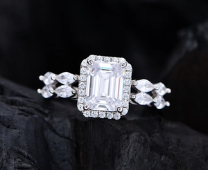 Macro view of emerald cut white stone with halo and marquise accents on silver band
