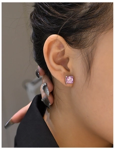 Close-up of pink square-cut diamond stud earring on ear with silver four-prong setting