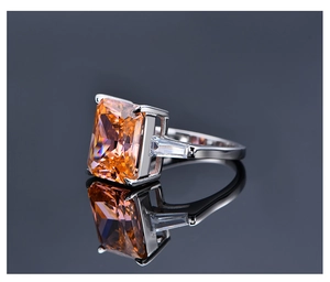 Vista macro de un anillo con gema naranja de 10,5ct y piedras laterales sobre espejo