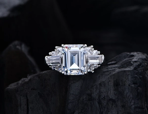 Macro detail of emerald-cut gemstone ring set with side stones on dark mineral background