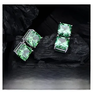 Close-up of 8ct square green emerald earrings with four-prong silver setting on dark stone