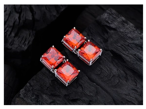 Detail of square red gemstone earrings in silver four-prong settings on charcoal background