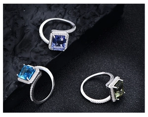 Detailed macro of three rectangle-cut emerald rings in blue and green on a dark rock