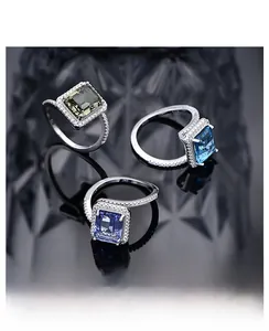 Macro detail of emerald-cut rings with green and blue stones on reflective black glass