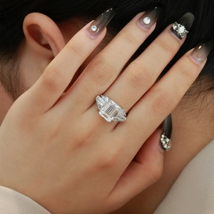 Elegant emerald-cut solitaire ring with side stones on a woman's finger, silver luxury band