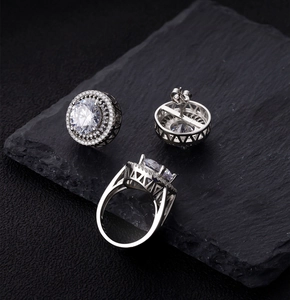 Close-up of 10mm round halo cut earrings and matching ring on black textured rock