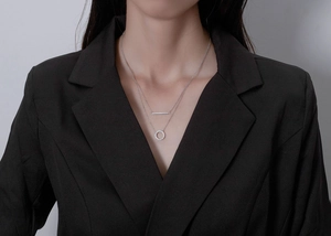 Macro detail of a double-layered silver necklace with bar and pavé circle pendant