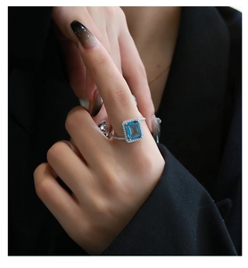 Detailed close-up of emerald-cut blue gemstone ring with halo diamond setting on model
