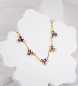 Detail of 18k gold necklace with purple gemstone snowflake charms on white floral stand