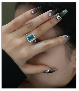 Macro detail of emerald-cut blue gemstone ring with pave diamonds on model hand