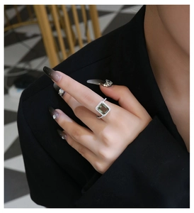 Detailed view of an emerald cut green stone ring with pavé diamonds on a model
