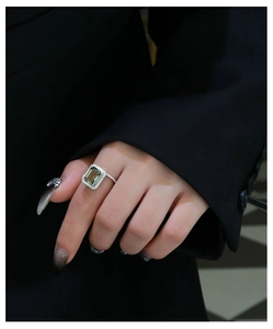 Close-up of an emerald cut green stone ring with pavé diamonds on a model's finger
