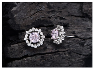 Close-up of pink gem stud earrings with silver lace halo setting on dark wood
