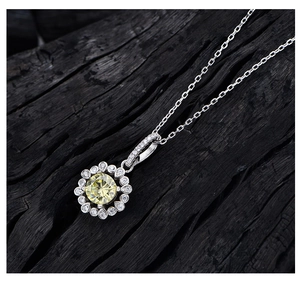 Detailed close-up of a silver floral pendant set with a 6mm yellow gem on black wood