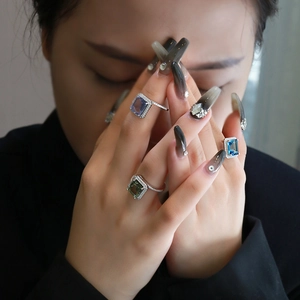 Three emerald cut halo rings with colorful stones worn on hand with long gradient nails