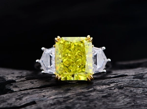 Macro detail of three-stone ring featuring radiant-cut yellow gem on black charred wood