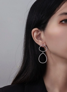 Gros plan de boucles d'oreilles géométriques argentées portées avec zircons étincelants